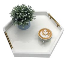 White hexagon serving tray with polished metal handles on a modern coffee table, displaying candles and a small plant. 